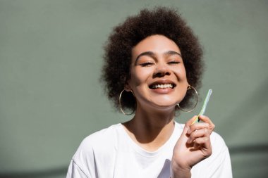 Neşeli Afrikalı Amerikalı kadın yeşil duvarın yanında jöleli pipet tutuyor.