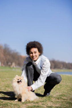 Mutlu Afrikalı Amerikalı kadın parkta Pomeranian köpeğine sarılıyor.