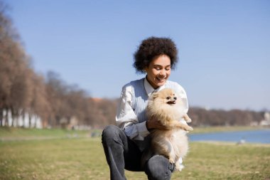 Pomeranian köpeğini elinde tutan neşeli Afrikalı Amerikalı kadın.