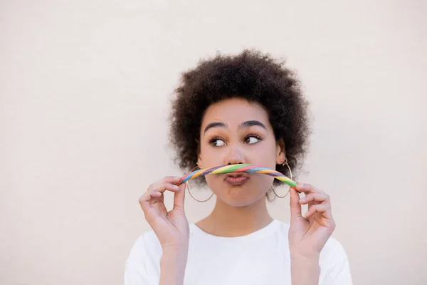 happy african american young woman grimacing and holding jelly candy on white