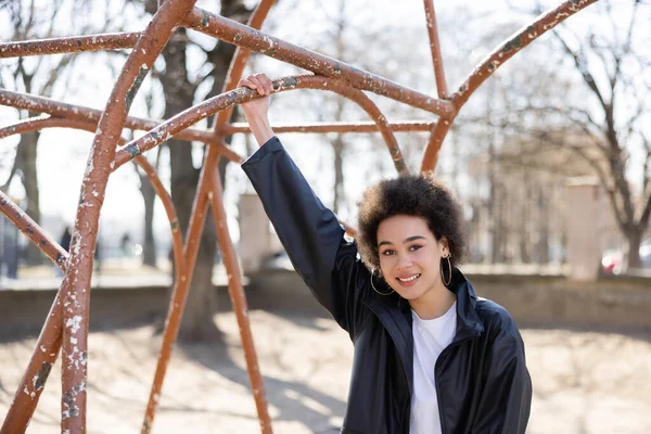 Paslı açık hava spor salonunda gülümseyen ceketli Afro-Amerikan kadın.
