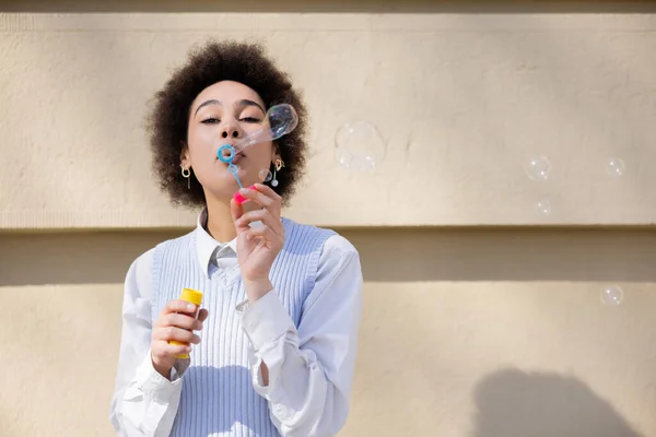 Curly African American Woman Holding Bottle Blowing Soap Bubbles Wall — Stockfoto