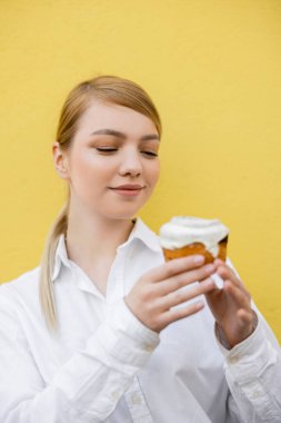 Sarışın, beyaz gömlekli, bulanık kek tutan, sarıda izole edilmiş bir kadın.