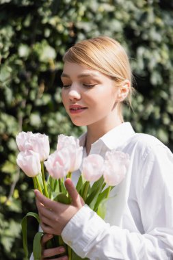 Bulanık arka planda beyaz laleler tutan mutlu sarışın kadın.