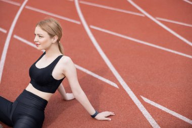 Spor sahasında oturan siyah sütyenli mutlu bir kadın.