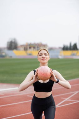 Güzel ve sportif bir kadın topla antrenman yapıyor ve kameraya bakıyor.