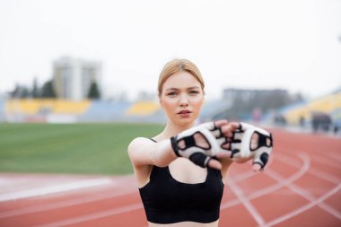 Siyah spor sutyenli ve spor eldivenli güzel bir kadın dışarıda ısınıyor.
