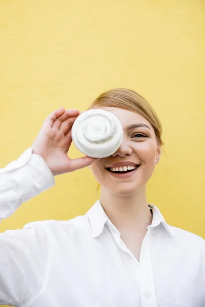 Cheerful Woman Covering Eye Cupcake While Smiling Camera Isolated Yellow — Stock Photo, Image