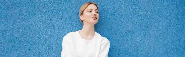 Усміхнена Жінка Білому Светрі Дивлячись Далеко Біля Синьої Стіни Банер — стокове фото
