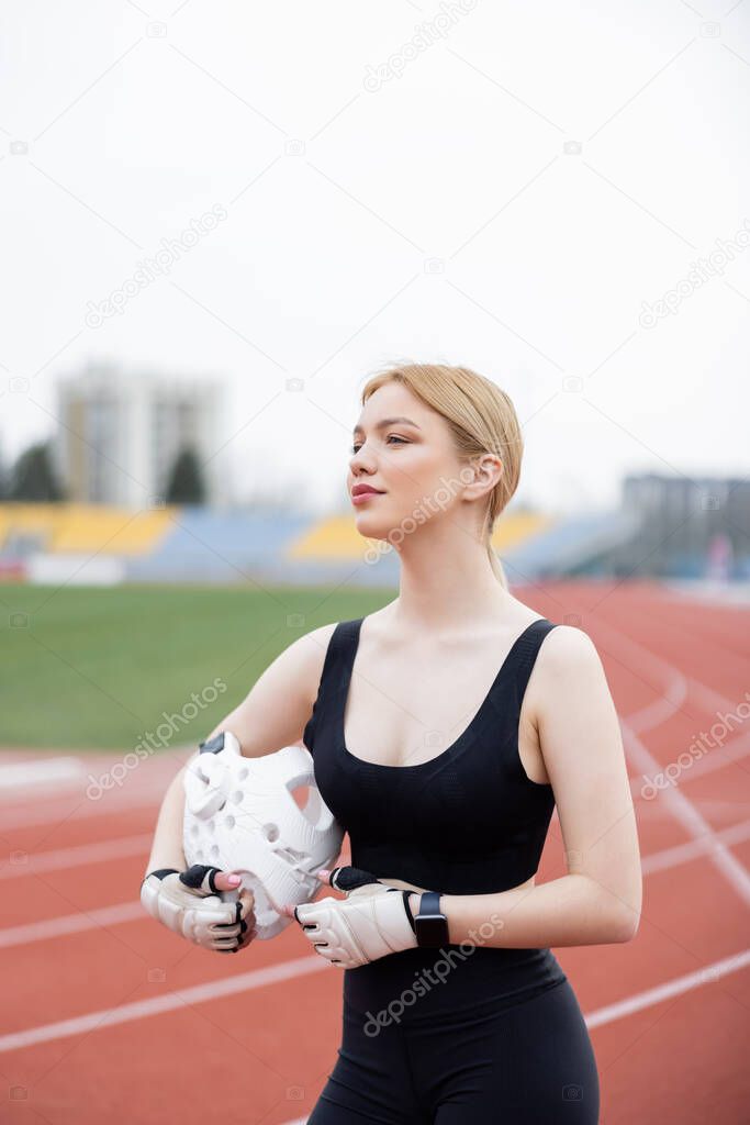 sportswoman in fitness gloves holding sports helmet and looking away outdoors