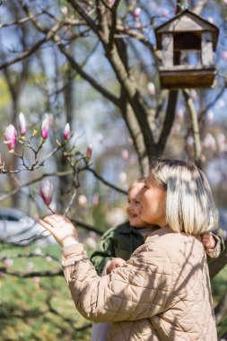happy mother and daughter looking at blossoming magnolia tree in park