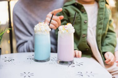 Caddedeki kafede, kızının yanında milkshake ile bardakları gösteren bir kadın manzarası.