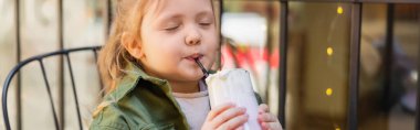 girl with closed eyes drinking delicious milk beverage outdoors, banner