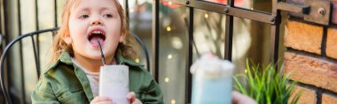 girl with open mouth holding glass of milkshake on blurred foreground, banner