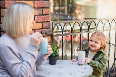 mother and daughter sitting with glasses of delicious milk cocktail in street cafe