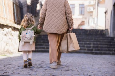 Alışveriş çantalı bir kadın ve sokakta yürüyen sırt çantalı bir kız.