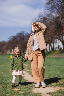 full length view of trendy woman looking away while walking with daughter in park