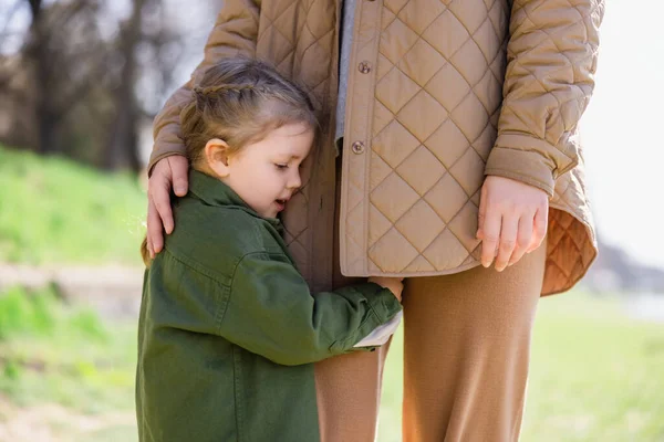 girl in trendy clothes embracing mother outdoors
