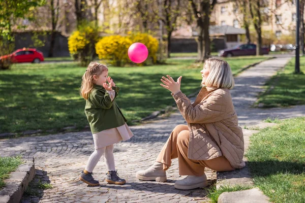side view of happy mother and child playing with ball in park