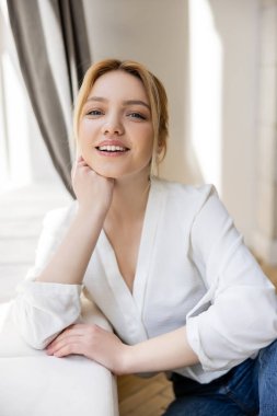 Evde kameraya bakan, bluzlu, neşeli sarışın kadının portresi. 