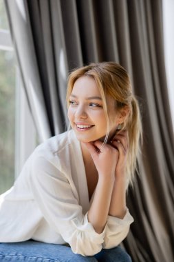 Evdeki bulanık pencerenin yanında oturan mutlu genç kadın. 