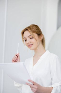 Elinde bulanık defter ve kalemle gülümseyen kadın. 