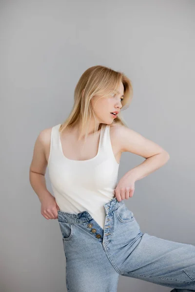 Blond Kvinna Body Suit Och Jeans Tittar Bort Isolerad Grå — Stockfoto