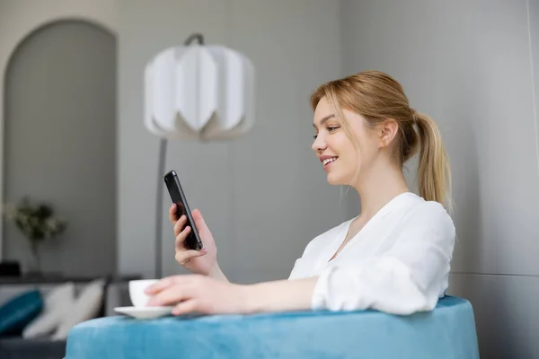 Mujer Joven Feliz Usando Teléfono Móvil Sosteniendo Taza Borrosa Sillón Imágenes De Stock Sin Royalties Gratis