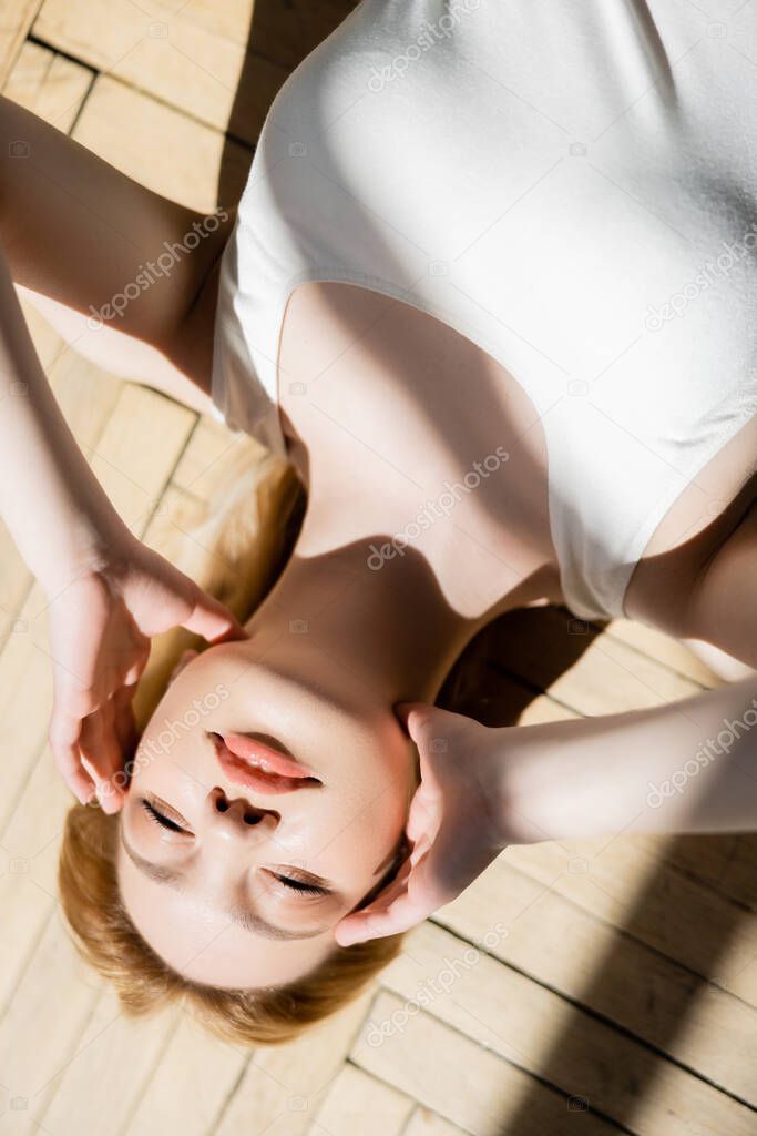 Top view of young woman touching face while lying on wooden floor at home 