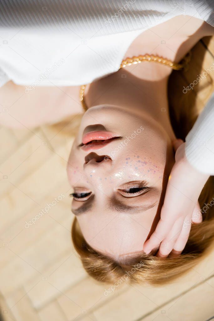 Top view of blonde woman with glitter on face looking at camera 