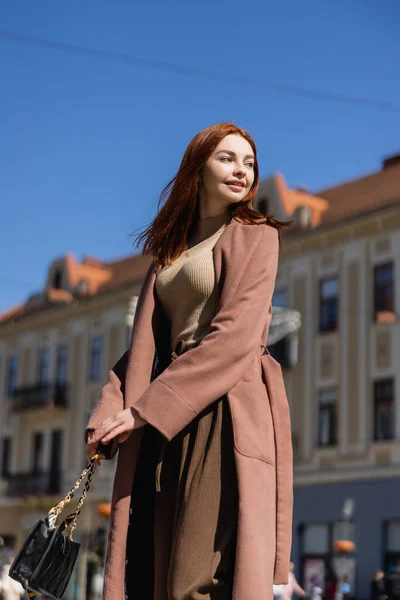 Vista basso angolo di donna rossa sorridente in cappotto sulla strada della città urbana europea — Foto stock