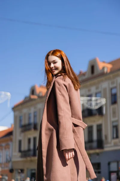 Fröhliche rothaarige Frau im Mantel auf der Straße der europäischen Stadt — Stockfoto