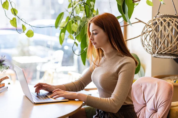 Young redhead woman using laptop in cafe — Stock Photo