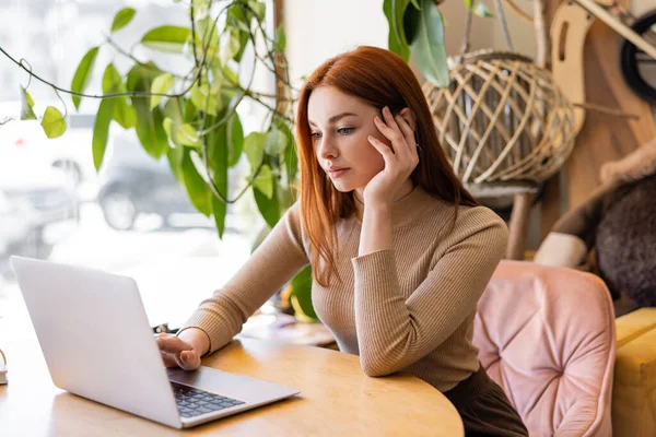 Young redhead freelancer using laptop in cafe — Stock Photo