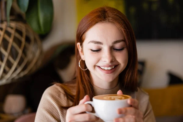 Junge fröhliche Frau lächelt und hält eine Tasse Latte im Café — Stockfoto