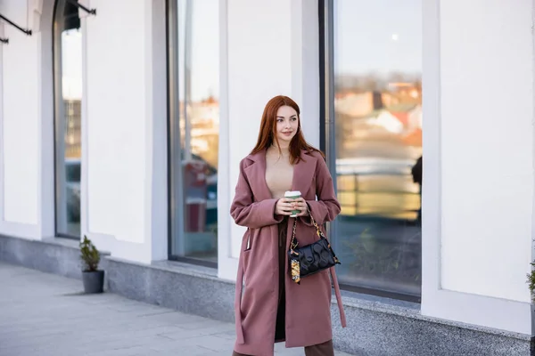 Rothaarige junge Frau mit Handtasche hält Pappbecher auf der Straße — Stockfoto