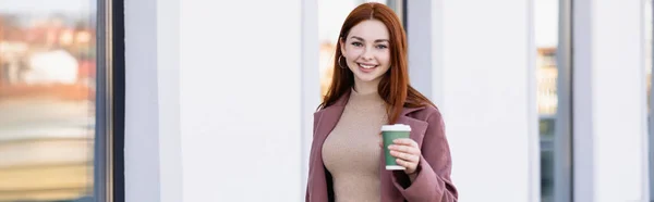 Cheerful woman holding coffee to go on urban street, banner - foto de stock