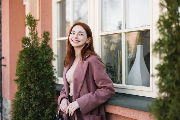 Young cheerful woman with red hair standing near building — Stock Photo