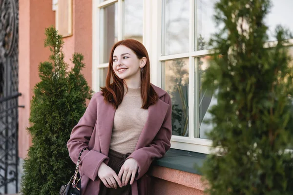 Young pleased woman with red hair standing near building — Stock Photo