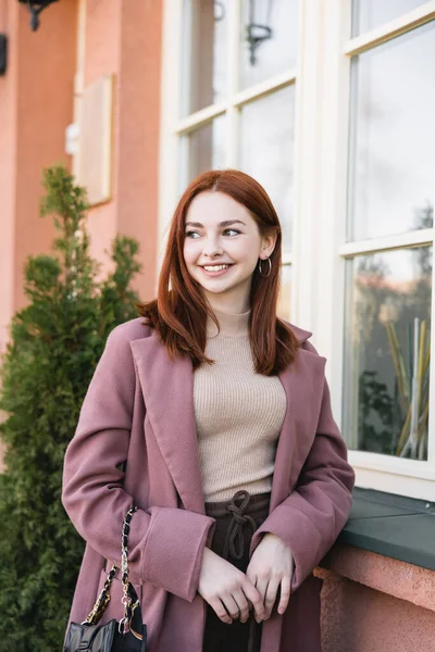 Jeune femme heureuse aux cheveux roux souriant près du bâtiment à l'extérieur — Photo de stock