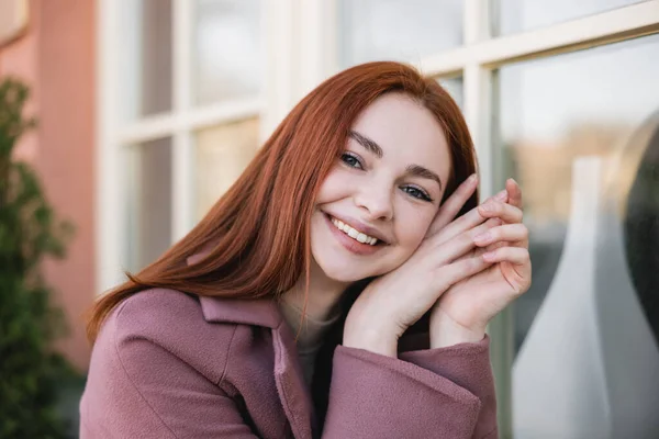 Portrait de jeune femme gaie en manteau regardant la caméra à l'extérieur — Photo de stock