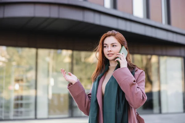 Joven pelirroja mujer en bufanda y abrigo hablando en el teléfono celular fuera - foto de stock