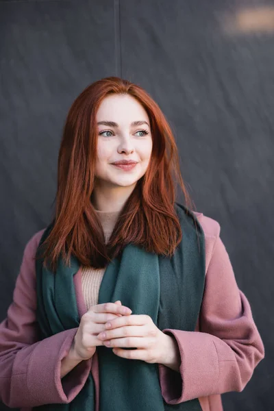 Mulher ruiva satisfeito em cachecol sorrindo perto de parede de mármore cinza — Fotografia de Stock