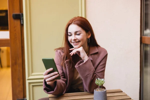Happy woman with red hair using smartphone on summer terrace — Stock Photo