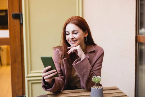 Happy woman with red hair using smartphone on summer terrace — Photo de stock