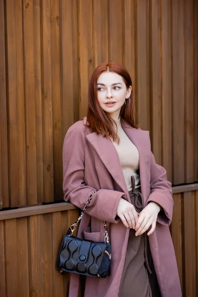 Jeune femme aux cheveux roux debout avec sac à main à l'extérieur — Photo de stock