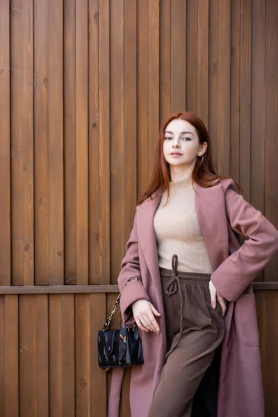 Heureuse jeune femme aux cheveux roux debout avec la main sur la hanche à l'extérieur — Photo de stock