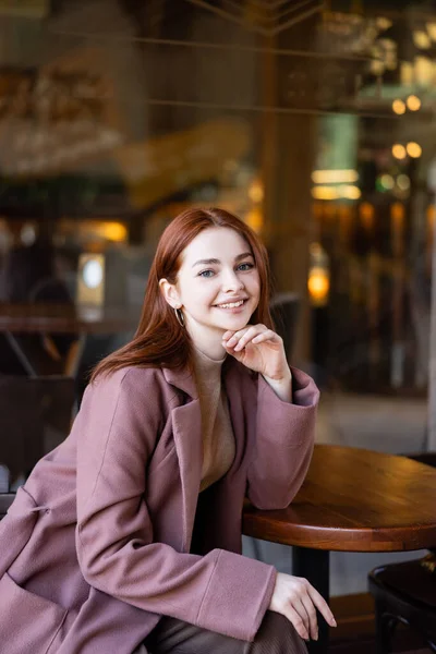Молода і щаслива жінка з рудим волоссям сидить на терасі кафе — стокове фото