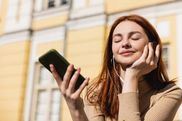 Mulher alegre ouvir música em fones de ouvido com fio e segurando smartphone — Fotografia de Stock