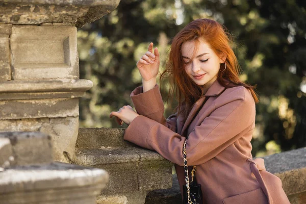 Junge glückliche rothaarige Frau im Mantel posiert draußen — Stockfoto